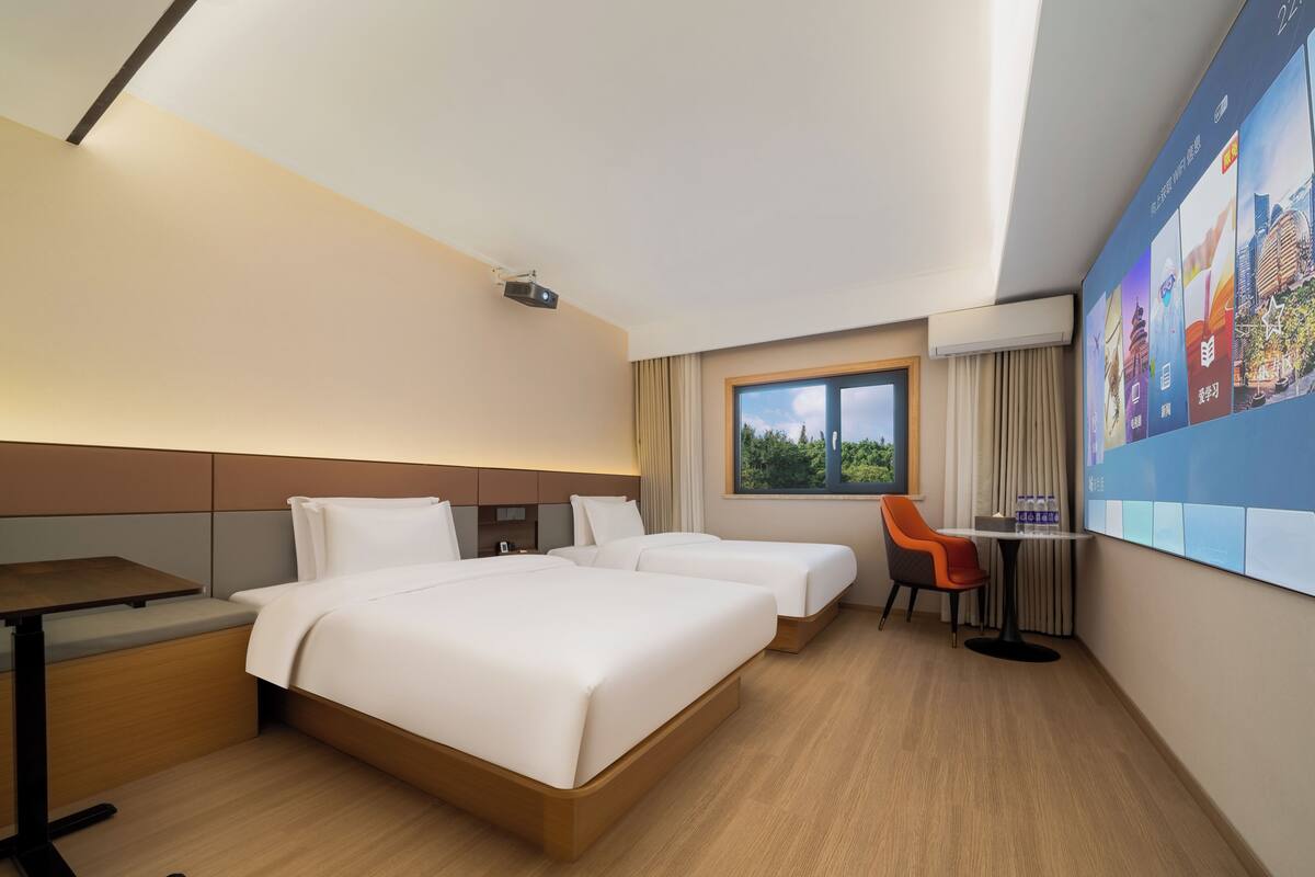 Habitación de hotel con dos camas, un escritorio, una silla, un televisor y ventana con vistas.
