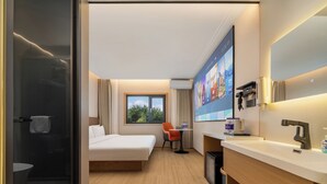 Ein Hotelzimmer mit Bett, Schreibtisch, Stuhl, Dusche und einem großen Fenster.