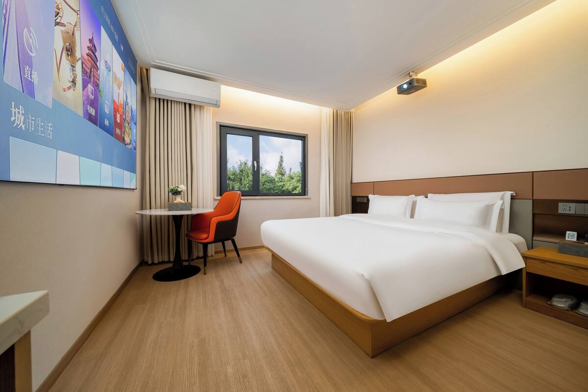 Una habitación de hotel con cama, un escritorio con silla, un ventanal y un proyector montado en la pared.