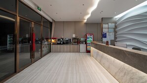 Eine moderne Hotelhalle mit Rezeption, Verkaufsautomaten und einem Glastür-Eingang.