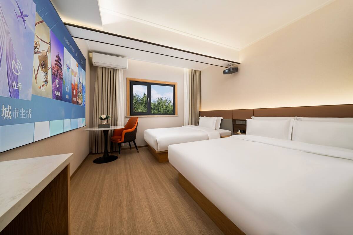 Habitación de hotel con dos camas, un escritorio, una silla, una ventana y una pared con carteles.