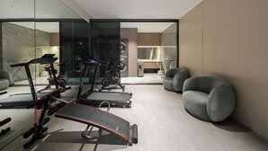 Ein moderner Home-Fitnessraum mit Trainingsgeräten, einem großen Spiegel und einer Sitzecke.