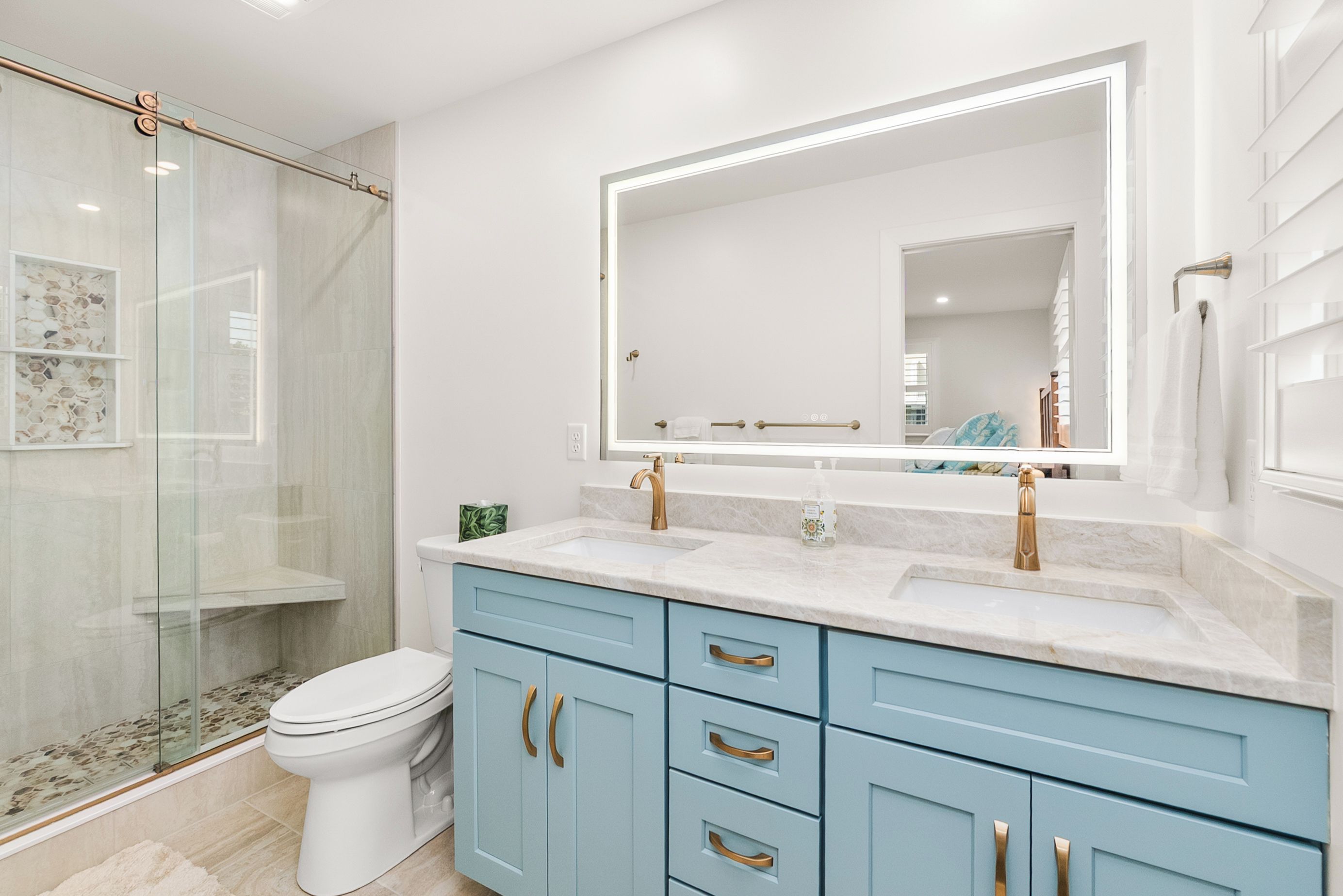 A bathroom with a glass shower enclosure, a toilet, a sink with a large mirror, and light blue cabinets.