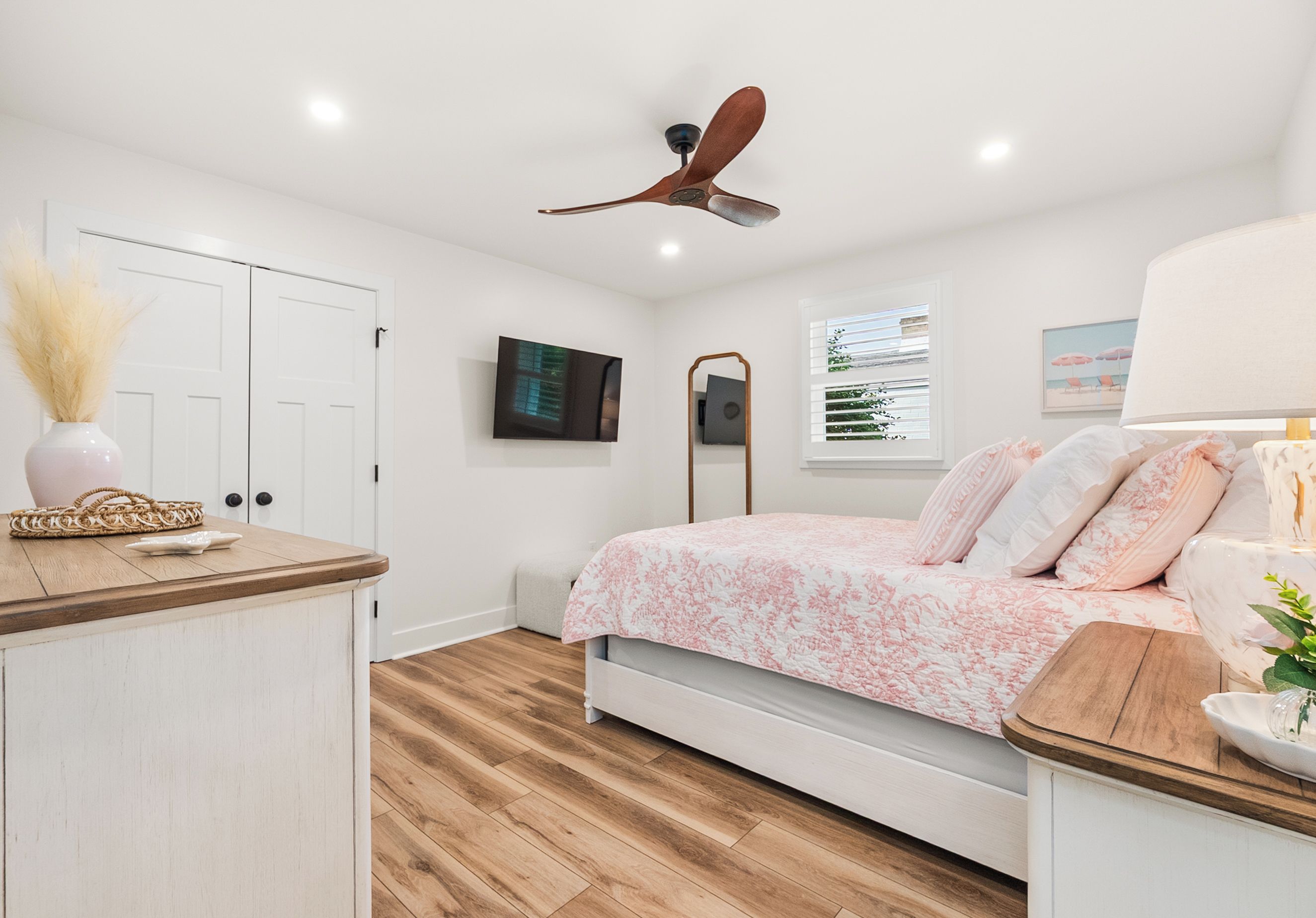 A bedroom with a bed, a ceiling fan, a TV, and a window with blinds.