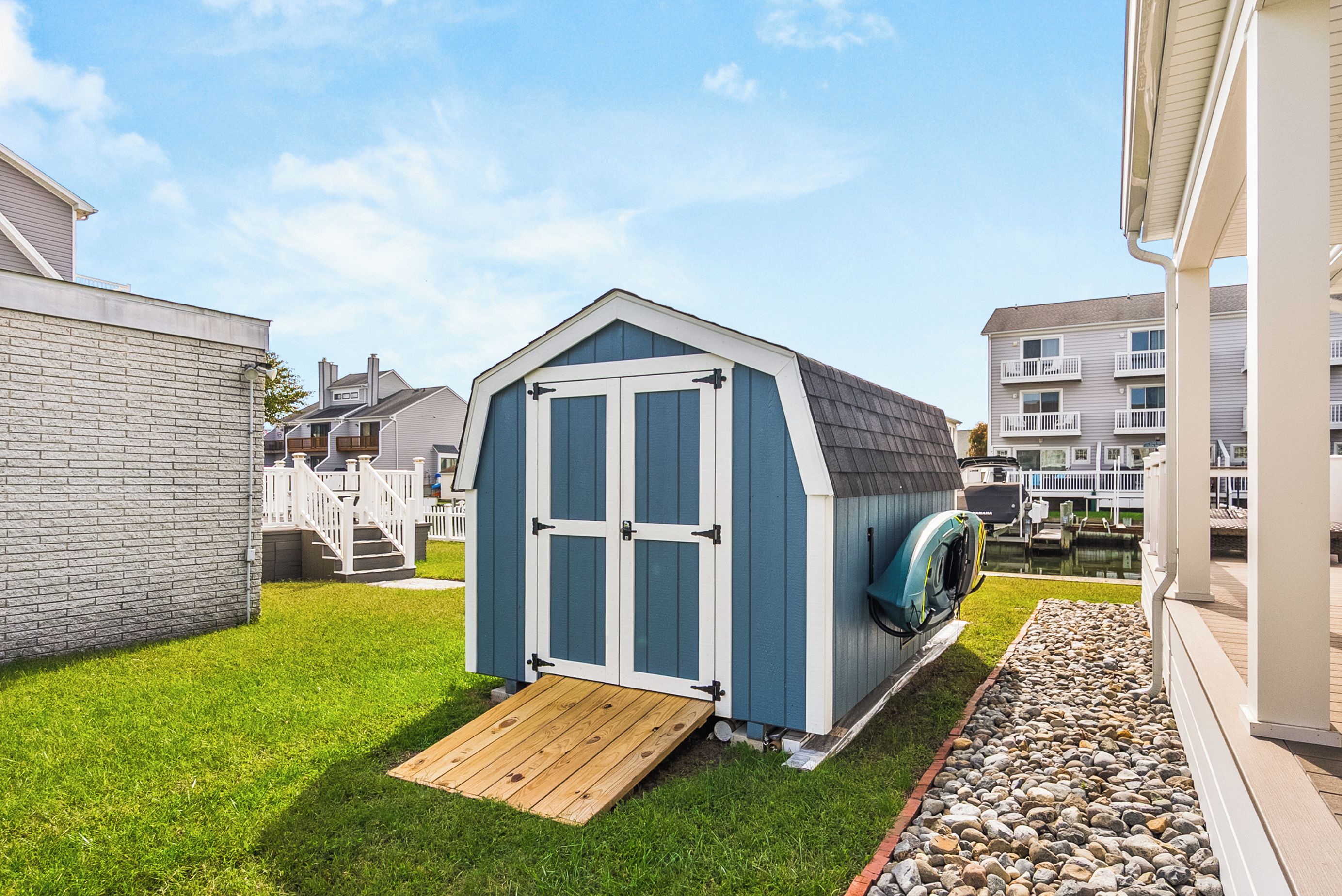 A small, single-story shed with a door and a ramp, surrounded by a well-maintained lawn and a gravel path.