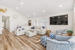 A modern living room with a sectional sofa, a patterned armchair, and a TV mounted on the wall. - Newly Renovated Bayside Retreat - Steps to the Beach (Ocean City)