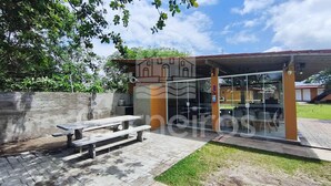 A covered outdoor seating area with a bench, a concrete wall, and a building with a glass entrance. - Flats Beira-rio com Espaco Gourmet Completo (Tamandaré)