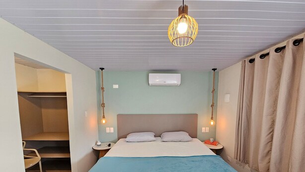 A hotel room with a bed, bedside tables, a hanging light fixture, a ceiling fan, and a window with curtains. - Flats Beira-rio com Espaco Gourmet Completo (Tamandaré)