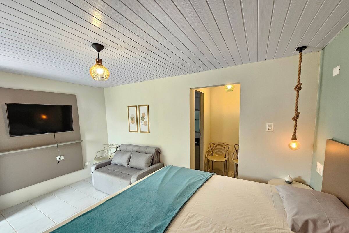 Un dormitorio con cama, televisor en la pared, sofá y sillón.