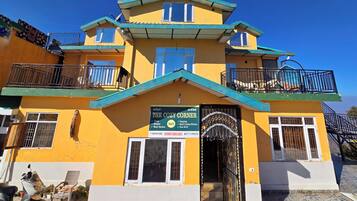 A multi-story building with a sign advertising "The Cozy Corner" and amenities like rooms, camping, and a back garden.