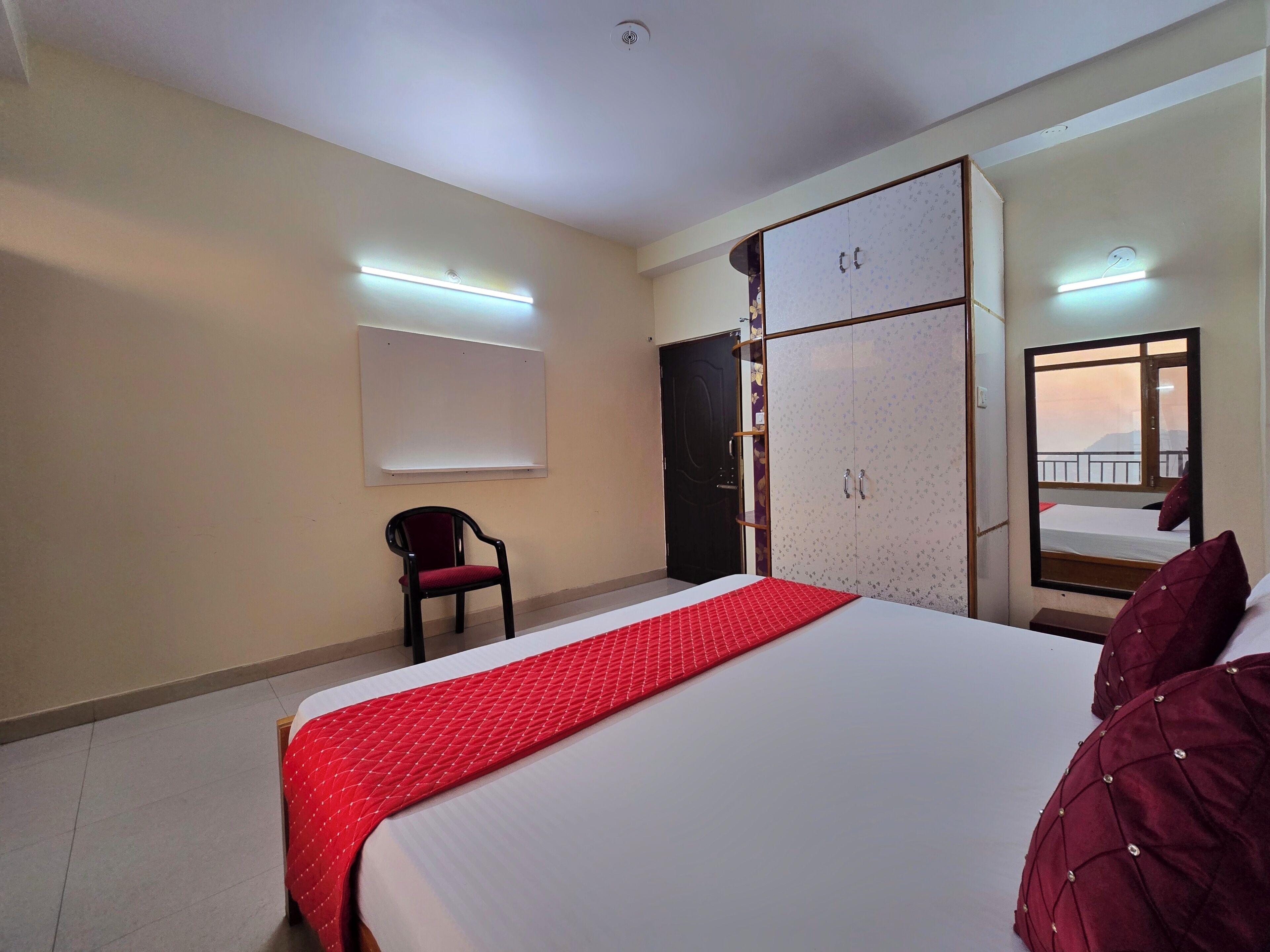 A hotel room with a bed, a wardrobe, a chair, and a mirror.