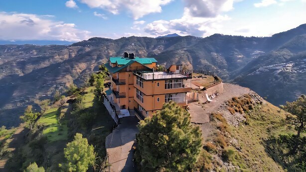 Um edifício de dois andares com telhado verde, localizado numa encosta com vista panorâmica das montanhas e vales circundantes.