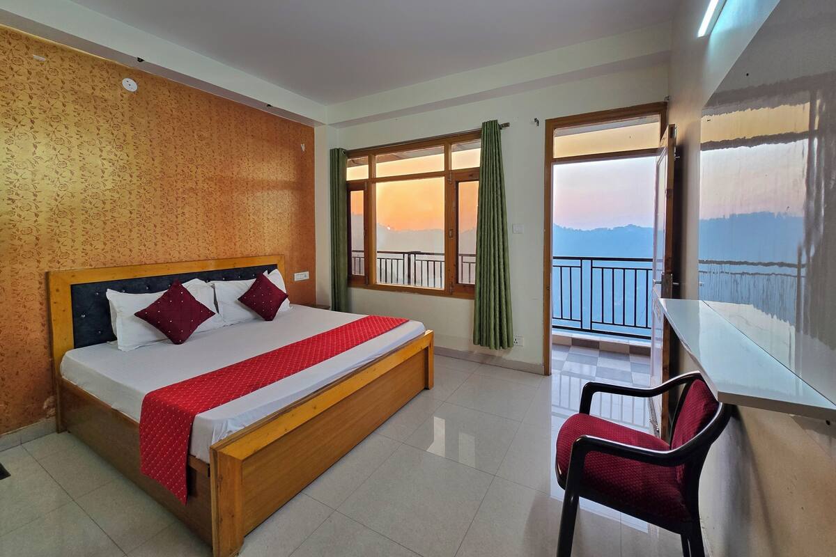 Ein Hotelzimmer mit Bett, Stuhl, einem Balkon mit Blick und einem fenster mit Vorhängen.
