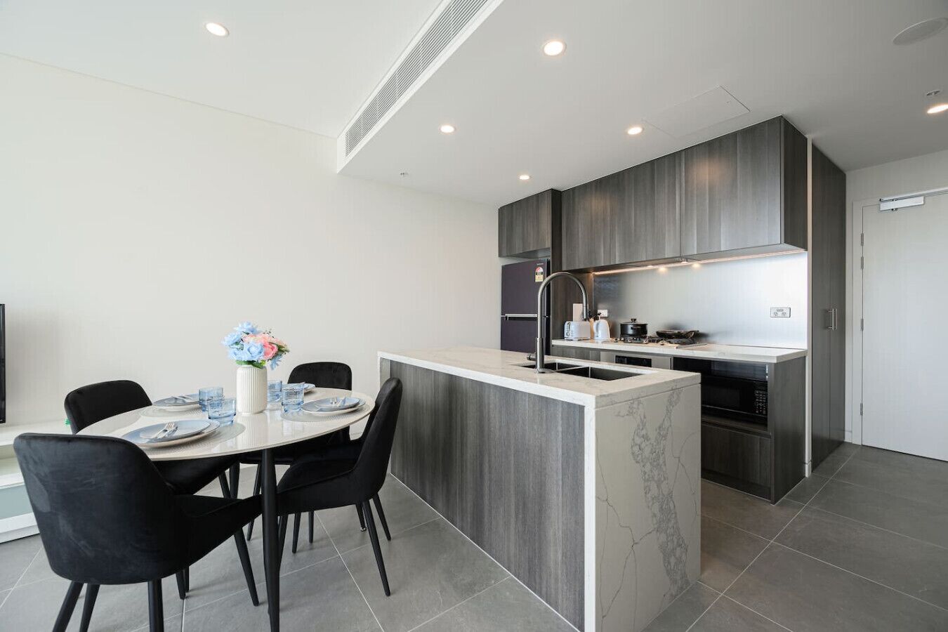 Une cuisine moderne dotée d’un îlot central, de meubles en bois foncé et d’un plan de travail blanc.