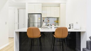 A modern kitchen with a central island, two bar stools, a refrigerator, and a coffee maker. - Modern 3-Bedroom Apartment Near Airport & Train (Mascot)