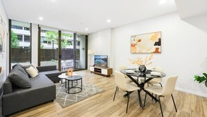 A modern living room with a sofa, dining table, and TV. - Modern 3-Bedroom Apartment Near Airport & Train (Mascot)