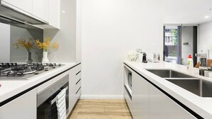 A modern kitchen with white cabinetry, a gas stove, a sink, and a countertop with a toaster and a bottle of dish soap. - Modern 3-Bedroom Apartment Near Airport & Train (Mascot)