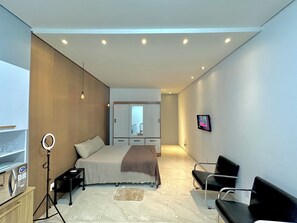 Een moderne slaapkamer met een bed, nachtkastje, lamp en een aan de muur bevestigde televisie.