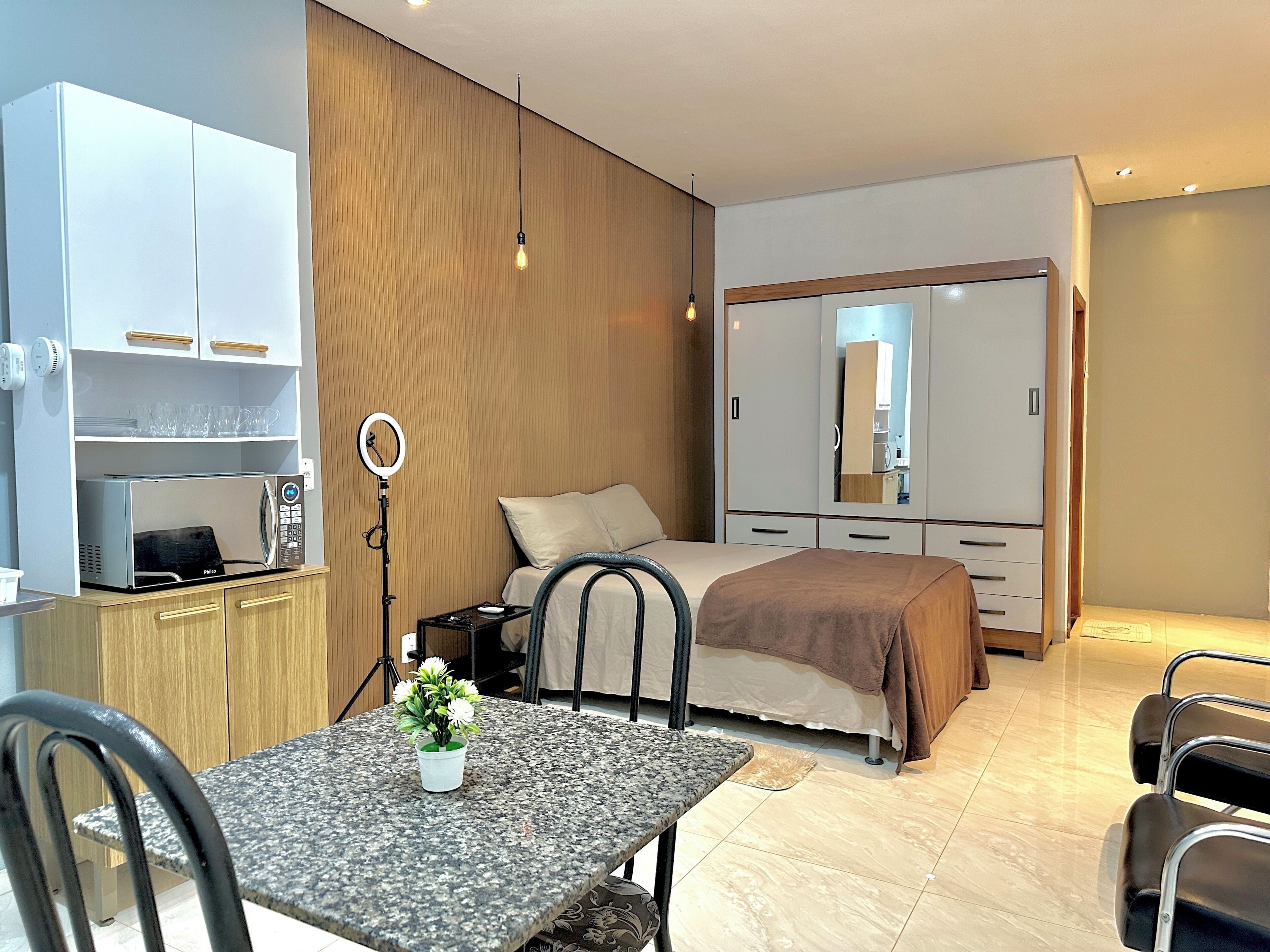 Un dormitorio moderno con cama, mesita de noche y una pequeña zona de escritorio con microondas.
