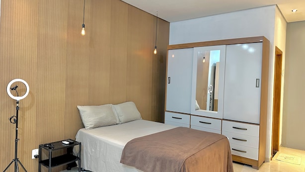 Un dormitorio con una cama, un armario, una luz de aro y una mesita.