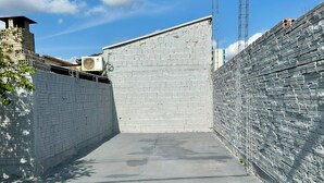 Un estrecho callejón con suelo de hormigón, flanqueado por paredes de ladrillo blanco y una cerca de metal en un lado.