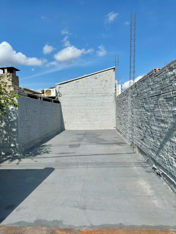 A narrow alleyway with a concrete floor, flanked by white brick walls and a metal fence on one side.