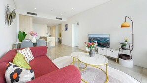 Ein modernes Wohnzimmer mit einem roten Sofa, einem weißen Couchtisch und einem Fernseher, der eine Stadtansicht zeigt.