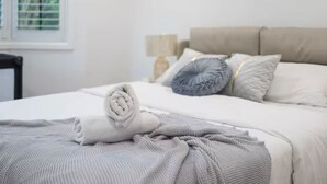 A neatly made bed with a rolled white towel, a grey blanket, and a grey pillow. - 4BR Castle Hill Home | Garage | Near Mall & Park (Castle Hill)