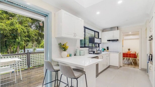 A modern kitchen with white cabinetry, a large island with bar stools, and a dining area with a red tablecloth. - 4BR Castle Hill Home | Garage | Near Mall & Park (Castle Hill)