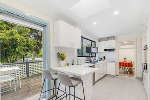 A modern kitchen with white cabinetry, a large island with bar stools, and a dining area with a red tablecloth. - 4BR Castle Hill Home | Garage | Near Mall & Park (Castle Hill)