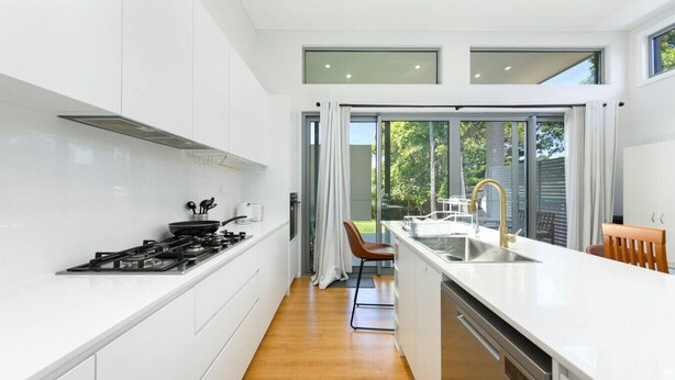 A modern kitchen with white cabinets, a stove, and a large window. - Modern Riverwood Home with Parking & Easy Access (Riverwood)