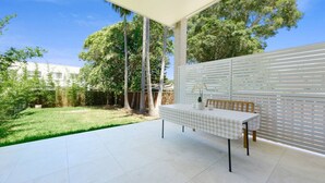 A patio with a checkered table and chairs, surrounded by a white fence and trees. - Modern Riverwood Home with Parking & Easy Access (Riverwood)