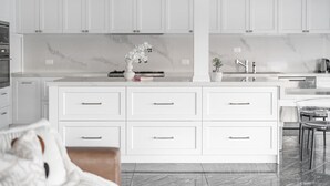 Una cocina moderna con armarios blancos, un protector contra salpicaduras de mármol y una isla central con cajones.