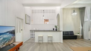Ein modernes Wohnzimmer mit Küchenbereich, einem schwarzen Sofa, einem kleinen runden Tisch und einem Fernseher links.