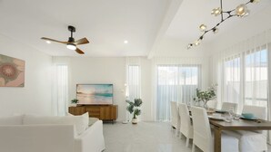 Una sala de estar moderna con un sofá, un comedor con una mesa y sillas, un ventilador de techo y un televisor sobre un mueble de madera.