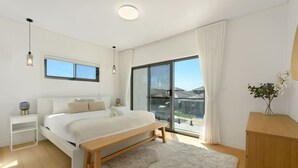 Un dormitorio moderno con una cama grande, un banco, una mesita de noche y vistas al exterior a través de un ventanal corredero.