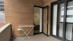 A balcony with a metal drying rack, a door leading to an interior space, and a tiled floor. - Burwood Studio 1Br Near Train Station/Shopping (Burwood)