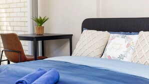 A neatly made bed with a blue bedspread and pillows, a small table with a woven basket and a plant, and a brown chair. - Botany 2Br Apt near Airport/Bay/City with 2Parking (Botany)
