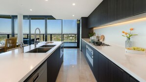 A modern kitchen with a large island, dark cabinetry, and a view of the city.