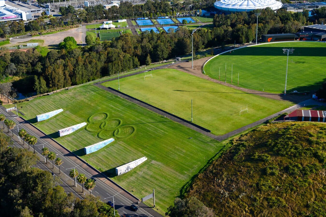 Luchtbeeld van een sportcomplex met meerdere velden, een stadion en omliggende gebouwen.