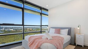 A modern bedroom with a large window, a bed with fluffy pink bedding, and a nightstand with a lamp.