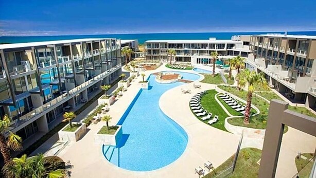 Um resort com piscina central, várias varandas e vista para o oceano.