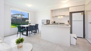 Une cuisine moderne avec des meubles blancs, un réfrigérateur, un four à micro-ondes et un évier. On y trouve également un coin repas avec une table et des chaises, ainsi qu’une fenêtre donnant sur l’extérieur.