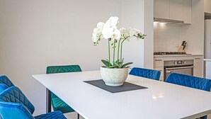 Un espace repas moderne avec une table blanche, des chaises bleues et un arrangement floral en guise de centre de table.