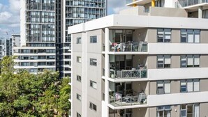 Un immeuble résidentiel moderne à plusieurs étages, doté de balcons, de grandes fenêtres et d’un espace de stationnement avec des voitures.