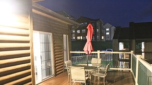A wooden deck with a glass table and chairs, a red umbrella, and a view of buildings in the background. - 2BD/2BA Condo next to Silver Dollar City (Branson)