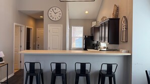 A modern kitchen with a bar area, featuring a clock, pendant lights, and dark cabinetry. - 2BD/2BA Condo next to Silver Dollar City (Branson)