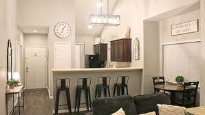 A modern kitchen with a bar area, a dining table with chairs, a sofa with cushions, and a clock on the wall. - 2BD/2BA Condo next to Silver Dollar City (Branson)