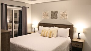 A neatly arranged bedroom with a large bed, two bedside tables, a nightstand, a sliding glass door, and three wall-mounted decorative panels. - 2BD/2BA Condo next to Silver Dollar City (Branson)