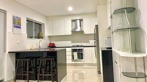 Una cocina moderna con armarios blancos, una isla central con taburetes, horno empotrado y estantería de vidrio.